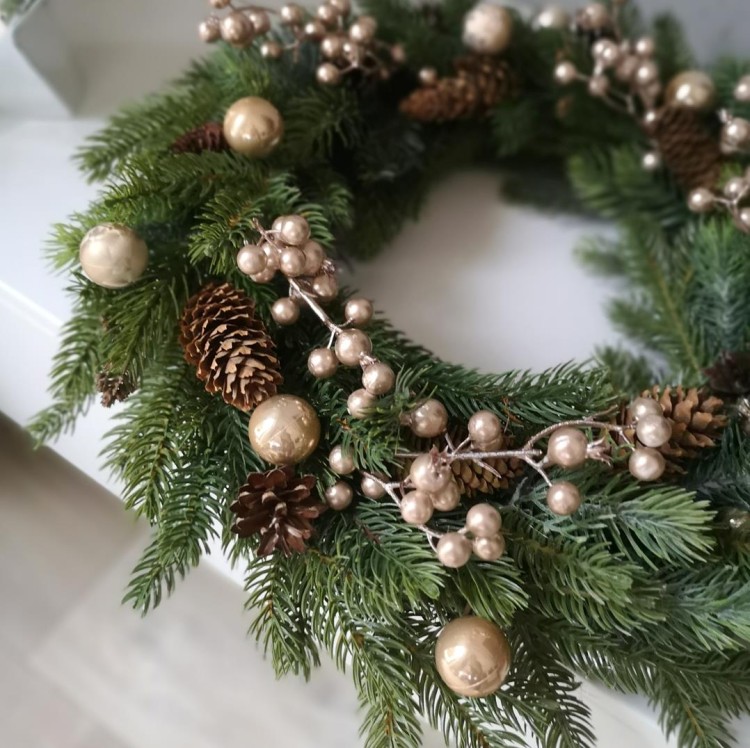 Świerkowy wianek z szyszkami, złotymi bombkami i złotymi jagodami.